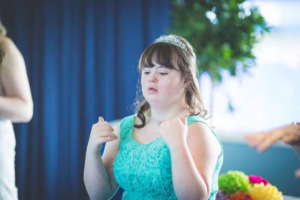 A young woman in a sea green sleeveless dress signs a song in British Sign Language. She is singing on of the 5 Great Wedding Readings