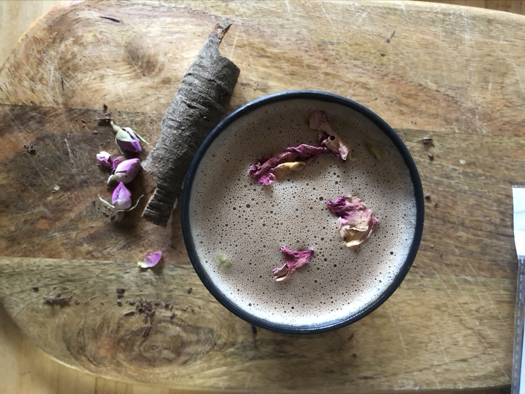 wooden board, stylised arial shot of a frothy hot chocolate with rose petals on top and a stick of cinnamon on the board to the left